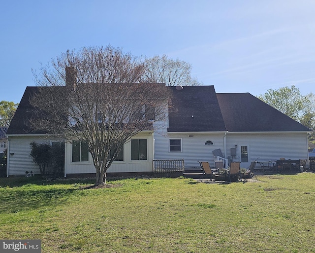 back of property featuring a lawn, roof with shingles, a chimney, and a deck