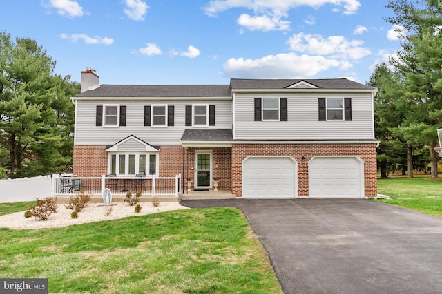 traditional-style home with aphalt driveway, fence, a front lawn, an attached garage, and brick siding