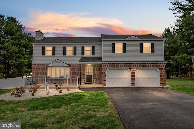 traditional home featuring a chimney, brick siding, an attached garage, a lawn, and aphalt driveway