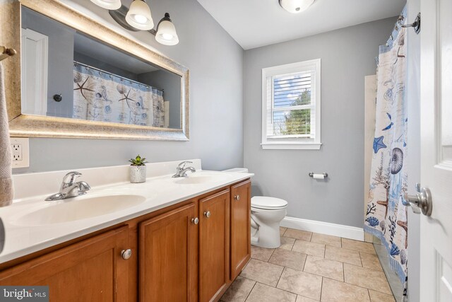 bathroom with double vanity, toilet, baseboards, and a sink