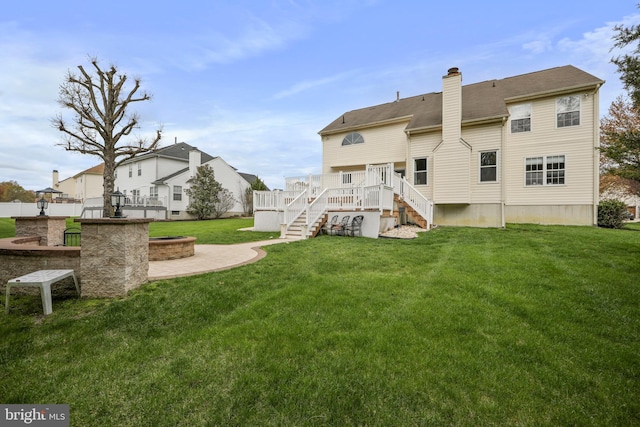 rear view of house featuring a chimney, a wooden deck, stairway, a yard, and an outdoor fire pit