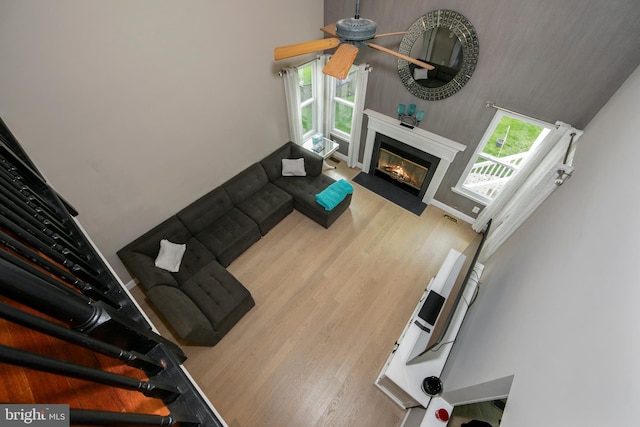 living area featuring a fireplace with flush hearth, a towering ceiling, wood finished floors, visible vents, and a ceiling fan