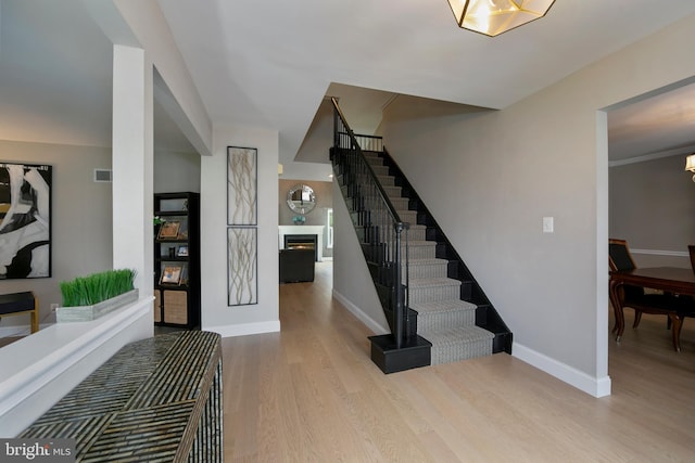 entryway featuring stairway, wood finished floors, visible vents, baseboards, and a lit fireplace