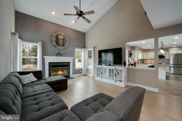 living area featuring high vaulted ceiling, a ceiling fan, light wood-style floors, a fireplace with flush hearth, and recessed lighting