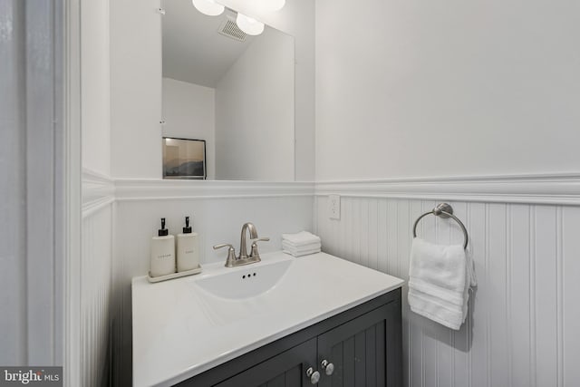 bathroom with vanity, a decorative wall, a wainscoted wall, and visible vents