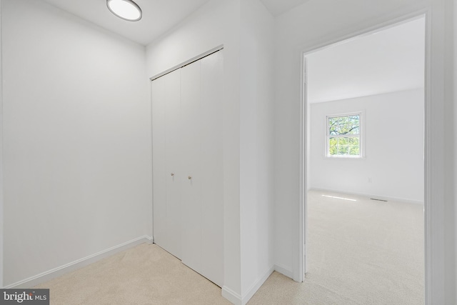 hall featuring baseboards and light colored carpet