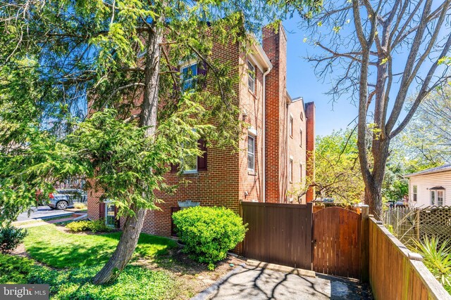 view of home's exterior with a gate, brick siding, a chimney, and fence