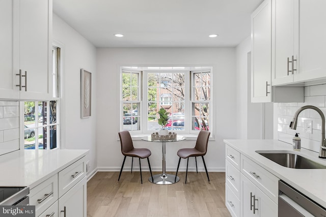 kitchen featuring light wood finished floors, dishwasher, a sink, baseboards, and white cabinetry