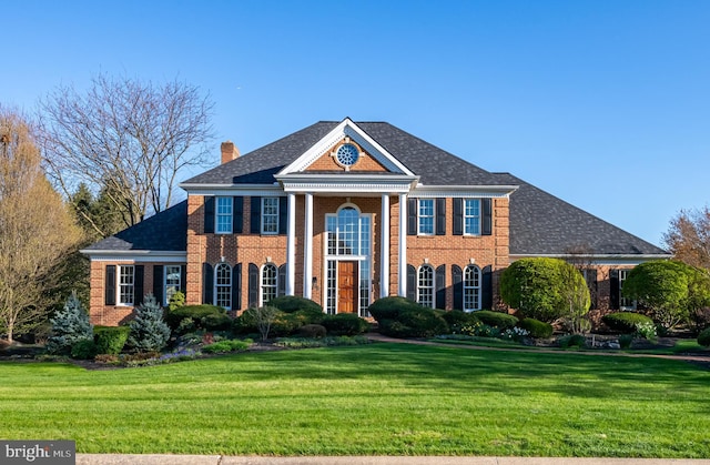 greek revival house featuring a chimney, brick siding, and a front yard