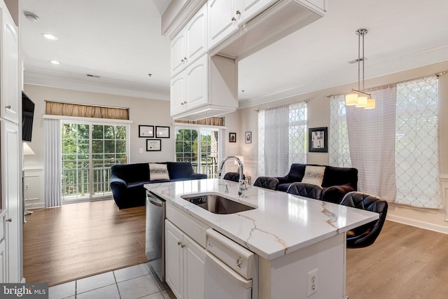 kitchen with white cabinets, a sink, a center island with sink, open floor plan, and ornamental molding