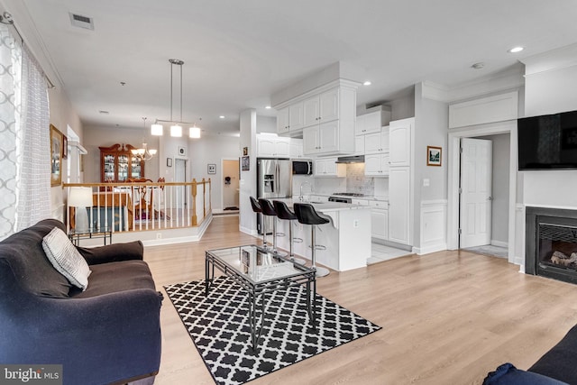 living area featuring a glass covered fireplace, visible vents, light wood-style flooring, and a notable chandelier