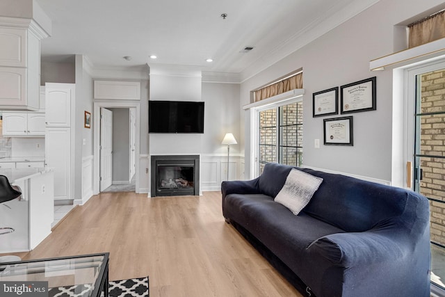 living room featuring ornamental molding, a glass covered fireplace, light wood-style floors, recessed lighting, and a wainscoted wall