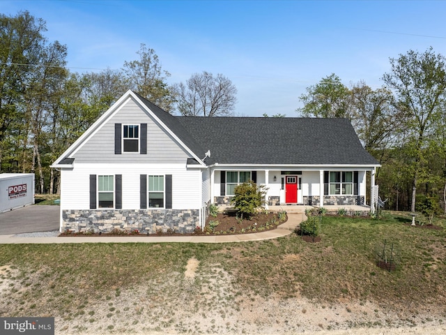 view of front facade featuring a porch, a front yard, stone siding, and a shingled roof