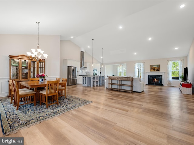 dining space with recessed lighting, a notable chandelier, high vaulted ceiling, light wood-style flooring, and a lit fireplace