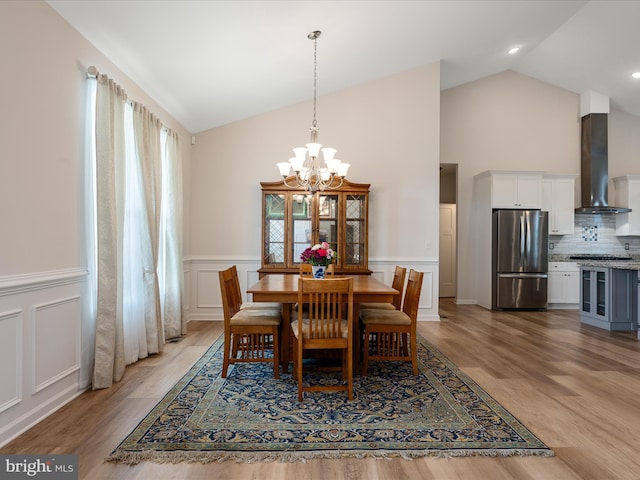 dining room with high vaulted ceiling, an inviting chandelier, light wood-style floors, and wainscoting