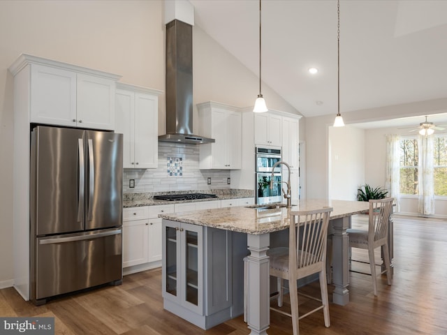 kitchen featuring a sink, appliances with stainless steel finishes, wall chimney exhaust hood, wood finished floors, and backsplash