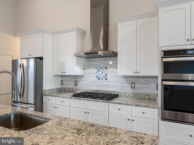 kitchen with white cabinetry, a sink, appliances with stainless steel finishes, wall chimney exhaust hood, and backsplash