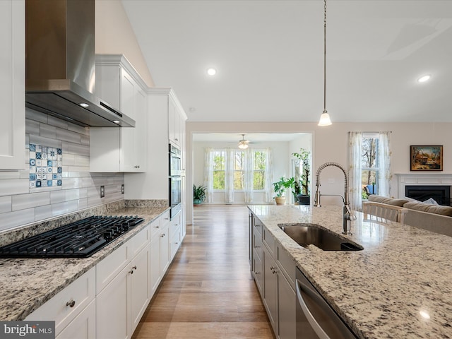 kitchen featuring a sink, stainless steel appliances, a fireplace, wall chimney exhaust hood, and open floor plan