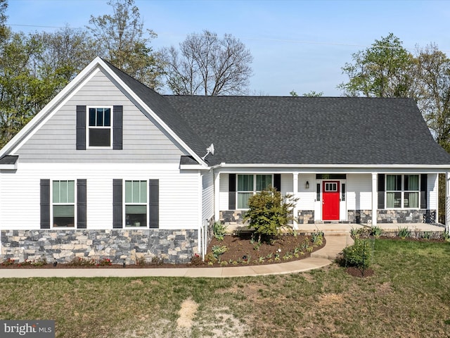 view of front of home featuring a front yard, stone siding, covered porch, and roof with shingles