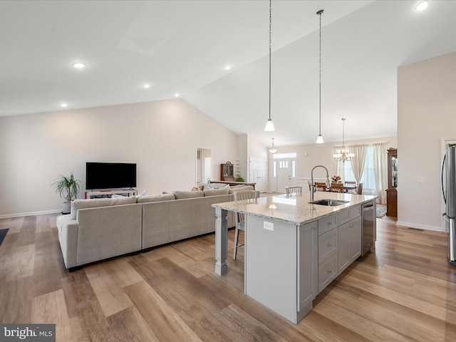 kitchen featuring light stone counters, a sink, stainless steel appliances, open floor plan, and vaulted ceiling