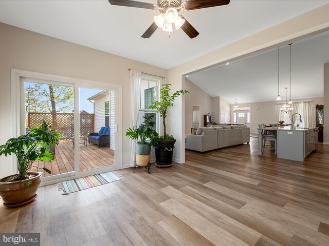 living area featuring lofted ceiling, wood finished floors, baseboards, and ceiling fan with notable chandelier