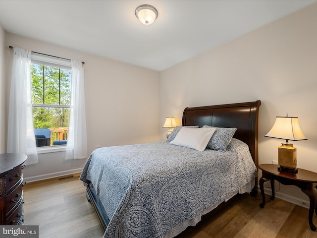 bedroom with baseboards, visible vents, and wood finished floors