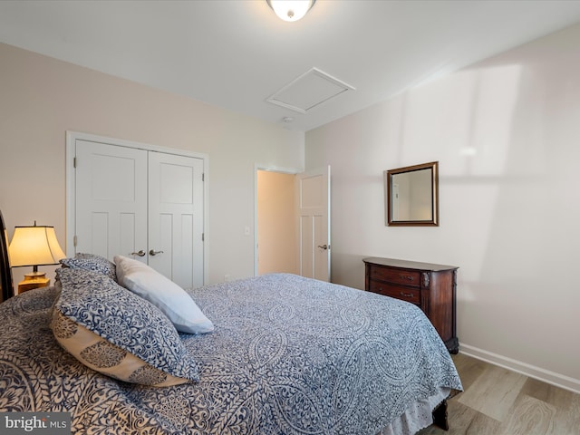 bedroom featuring baseboards, light wood-type flooring, attic access, and a closet