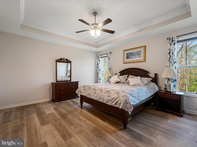 bedroom featuring baseboards, wood finished floors, crown molding, and a tray ceiling