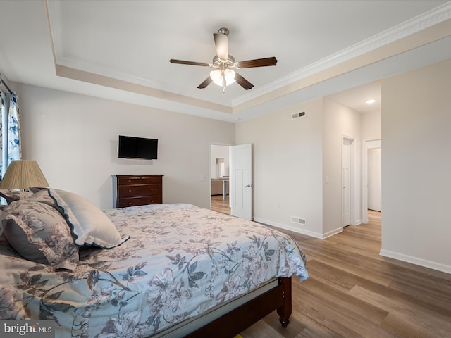 bedroom with visible vents, ornamental molding, wood finished floors, and a tray ceiling