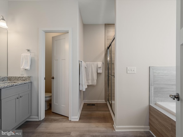 bathroom featuring a stall shower, toilet, a bath, wood finished floors, and vanity