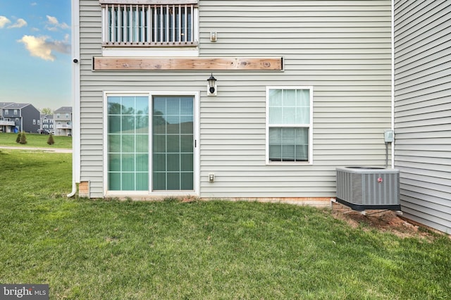 back of property with central AC unit, a balcony, and a lawn