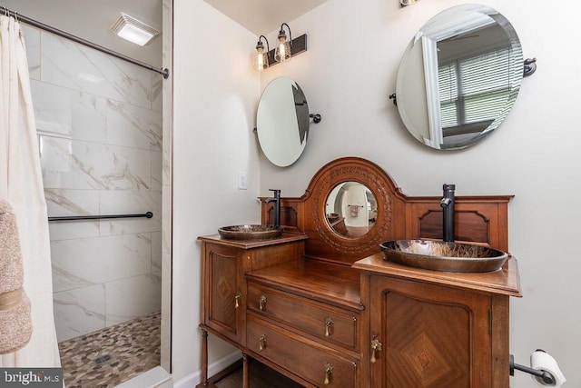 full bath featuring a tile shower, a sink, and double vanity
