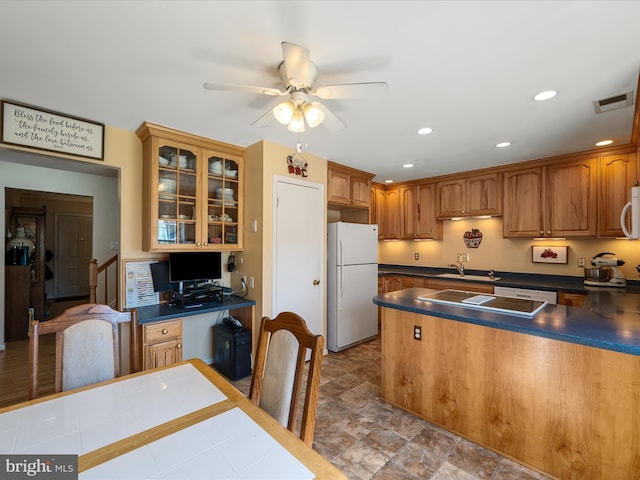 kitchen featuring dark countertops, a sink, white appliances, glass insert cabinets, and ceiling fan