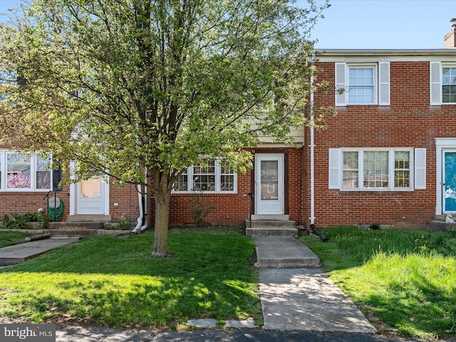 view of property featuring entry steps, a chimney, brick siding, and a front yard