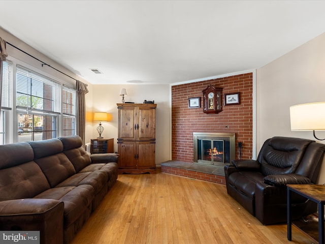 living area with light wood finished floors, a brick fireplace, and visible vents
