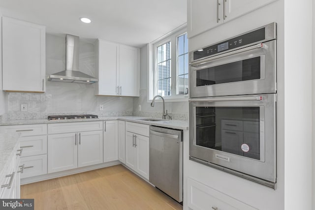 5634 6th St N, Arlington, VA 22205 - kitchen with wall chimney exhaust hood, appliances with stainless steel finishes, a sink, white cabinetry, and light stone countertops
