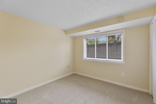 spare room with a textured ceiling, visible vents, baseboards, and light carpet