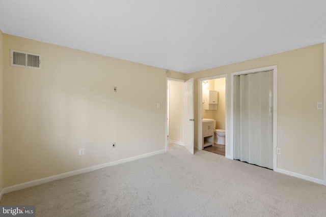 unfurnished bedroom featuring ensuite bath, visible vents, carpet flooring, and baseboards