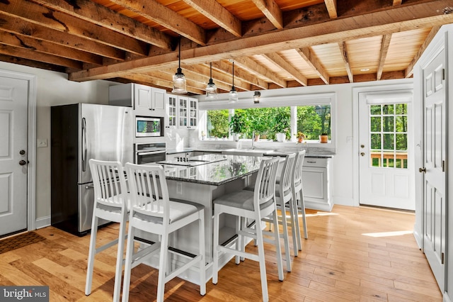 kitchen with glass insert cabinets, stone countertops, beamed ceiling, a kitchen bar, and stainless steel appliances