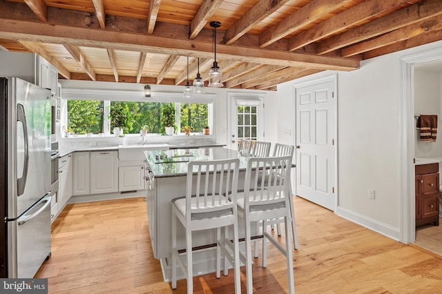 kitchen with appliances with stainless steel finishes, light stone counters, a sink, light wood-type flooring, and beamed ceiling