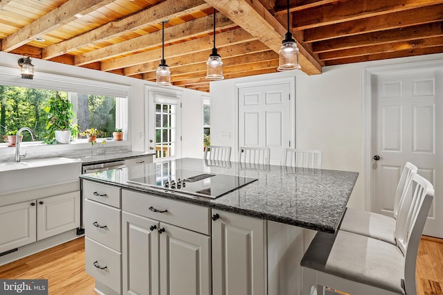 kitchen featuring white cabinets, black electric stovetop, a sink, light wood finished floors, and a center island