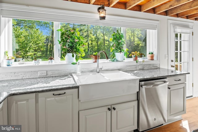 kitchen featuring stainless steel dishwasher, light stone countertops, a wealth of natural light, and a sink