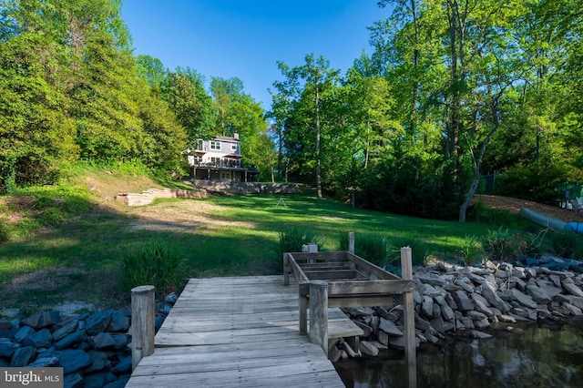 view of dock with a lawn, a water view, and a wooded view