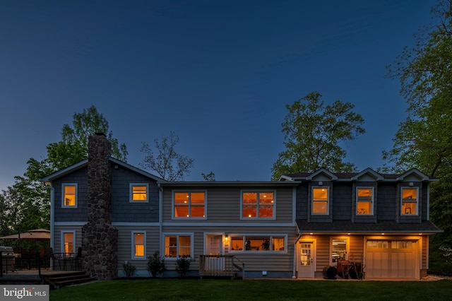 rear view of property featuring an attached garage, a yard, and a chimney