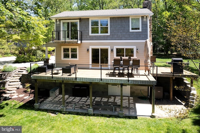 back of property with a balcony, outdoor dining area, a patio, a chimney, and a lawn