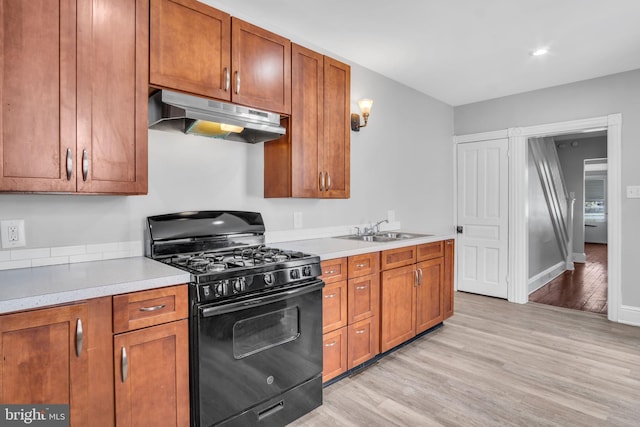 kitchen with brown cabinetry, light wood-style floors, under cabinet range hood, a sink, and black range with gas cooktop