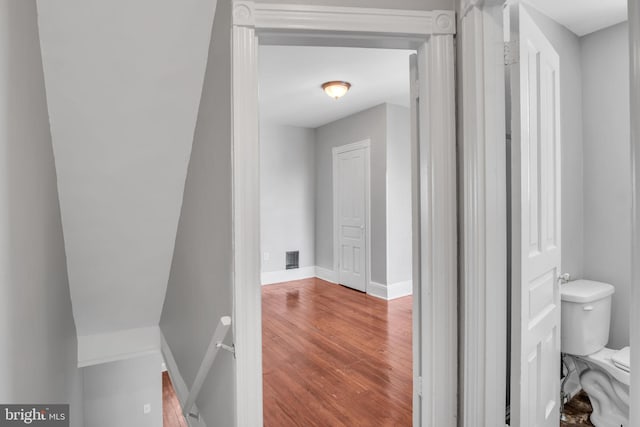 hallway with baseboards, wood finished floors, visible vents, and an upstairs landing
