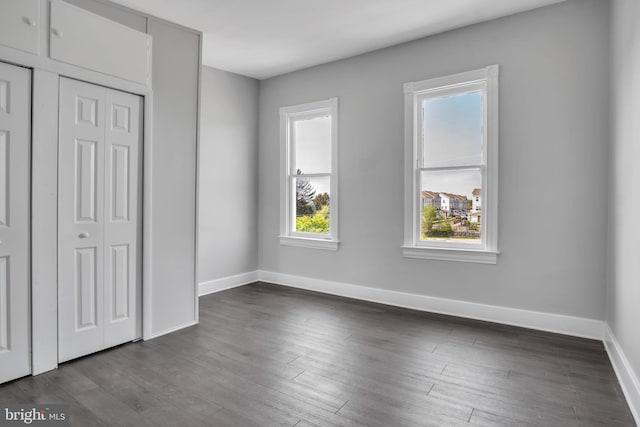 unfurnished bedroom with baseboards, dark wood-type flooring, and a closet