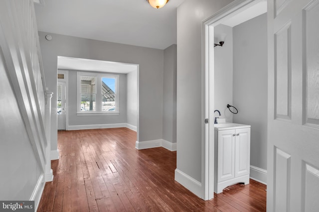 hall featuring a sink, baseboards, and dark wood finished floors
