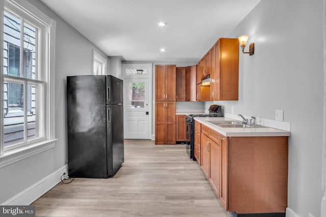 kitchen with brown cabinetry, a sink, light countertops, black appliances, and light wood finished floors